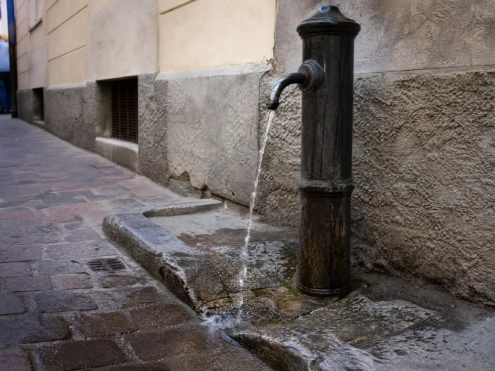 A cast-iron street fountain running onto worn stone